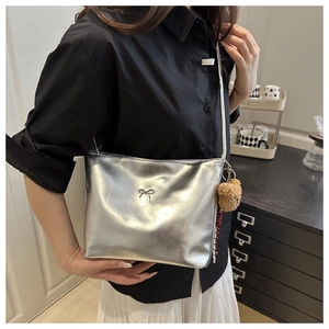 Silver metallic tote bag with bow detail and bear charm shown on model in home setting