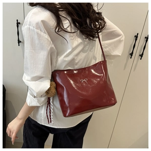 Detail of glossy deep red shoulder bag with silver bow and plush bear charm