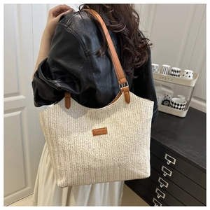 Detail of a large woven straw tote bag featuring a leather fashion tag and brown straps