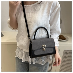 Detail view of contrast color crossbody bag featuring a golden horseshoe clasp and woven flap