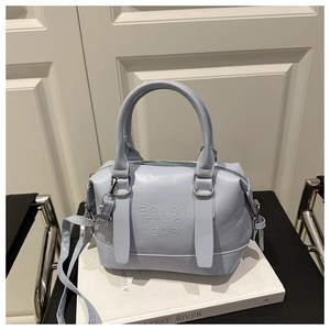Détail du sac Boston en similicuir bleu clair avec gaufrage posé sur des livres blancs