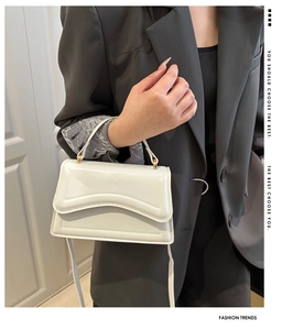 Close-up of a white wave-flap handbag with gold metal hardware and fine leather texture