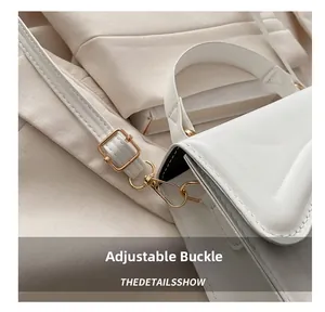 Detail shot of the golden metal buckle and adjustable shoulder strap on a white bag
