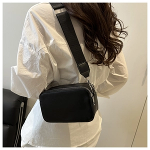 Detail of black crossbody camera bag featuring silver zippers and wide fabric strap