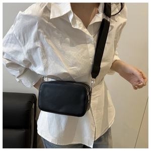 Detail of a chic black camera crossbody bag styled with a white shirt and denim