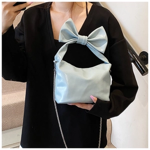 Detail of light blue glossy tote bag featuring a large bow and silver chain strap