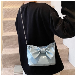 Detailed close-up of a light blue glossy tote bag with a large decorative bow and silver chain