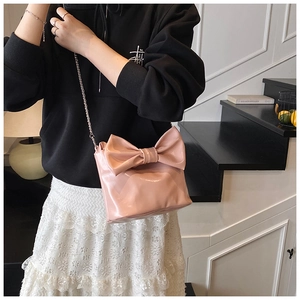 Pink bow-shaped shoulder bag in glossy patent finish shown worn by a model in a minimal setting