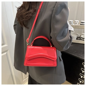 Detail view of red leather crossbody bag with wave stitching and gold hardware accents