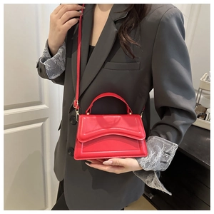 Detail of red leather crossbody bag featuring wavy flap and gold-tone hardware on a model