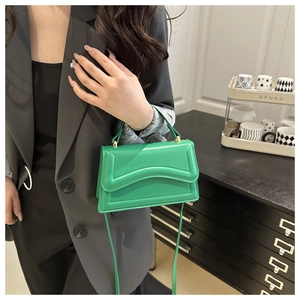 Detail of vibrant green leather handbag with wavy stitching and gold hardware on a model