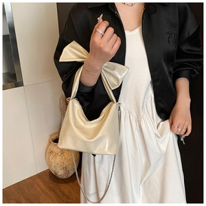 Detail of beige glossy tote bag featuring a decorative bow and silver chain strap