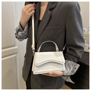 Close-up of a white textured crossbody bag with gold hardware worn on a grey suit