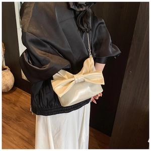 Detail of elegant beige tote bag with large bow design and thin metal chain strap