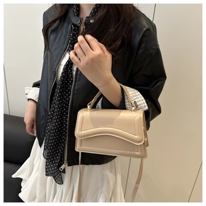 Side view of beige crossbody bag with wavy edge design worn with black jacket