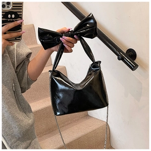Detail of black patent leather tote bag featuring a large oversized bow and chain strap