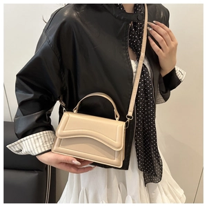 Detail of cream crossbody bag with leather jacket and pleated skirt outfit styling