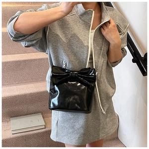 Close-up of black patent leather crossbody bag with oversized bow and silver chain strap