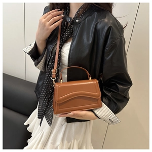 Close-up of brown leather crossbody bag with wave stitching detail and gold buckle hardware