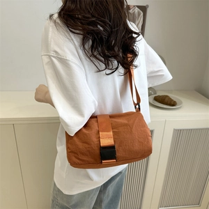 Sac bandoulière en nylon orange avec large sangle porté par un mannequin en intérieur