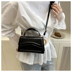 Model wearing a black leather crossbody bag with curved stitching and gold hardware detail