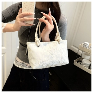 Detailed shot of white lace handbag featuring delicate butterfly embroidery and rope handles