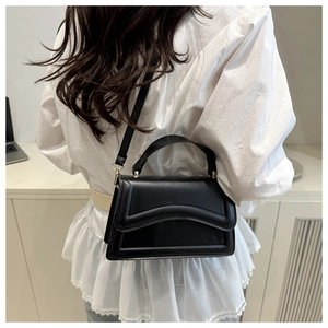 Detail of minimalist black leather crossbody bag featuring wave-pattern stitching and gold hardware