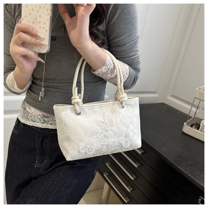 Detail view of intricate butterfly embroidery on cream lace fabric of a handheld bag
