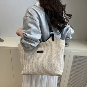 Minimalist straw tote bag with black leather straps and fashion tag on beige woven surface
