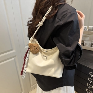 Large beige glossy hobo bag with metal bow and plush bear charm shown on model