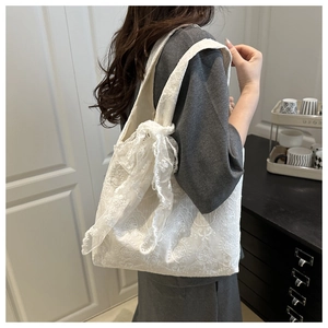 Détail du sac cabas en dentelle blanche avec motifs au crochet et nœud latéral élégant