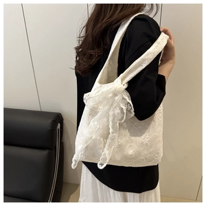 Close-up of intricate floral lace embroidery and side bow detail on a white tote bag