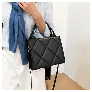 Detail of black quilted tote bag with gold metal hooks and adjustable shoulder strap