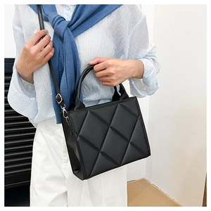 Detail of black quilted tote bag with diamond pattern and gold-tone metal hardware