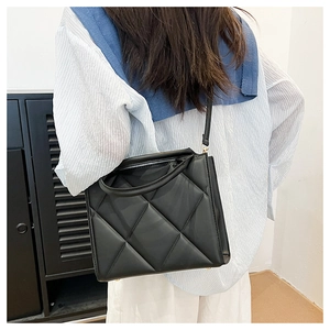 Detail of classic black quilted tote bag with gold hardware shown on a model's shoulder