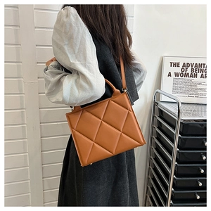 Brown quilted tote bag with large diamond patterns shown worn by a model in a studio
