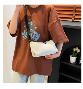 Detail einer cremeweißen Umhängetasche mit verstellbarem schwarzem Gurt am Model