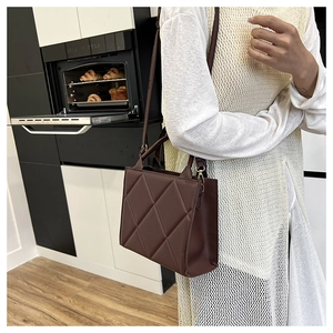 Close-up of brown quilted tote bag with gold hardware worn by a model in a modern kitchen