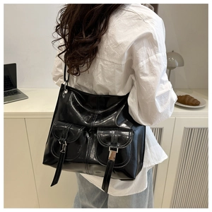 Detail of black glossy leather tote bag with functional front flap pockets and buckles