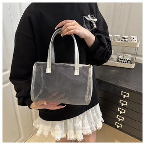 Detail of silver mesh tote bag with metallic handles held by a model in a casual setting