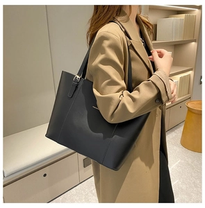 Minimalist black leather tote bag with gold buckle detail shown on a model