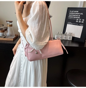 Pink baguette shoulder bag with pearl accents and heart pendant worn by a model