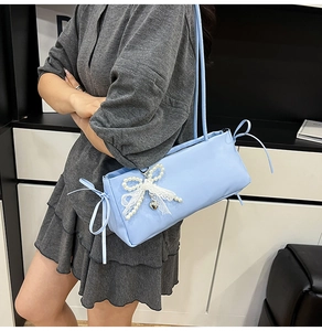 Close-up of light blue baguette bag featuring white lace, pearl bow and heart pendant