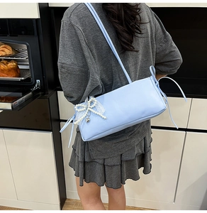 Close-up of light blue underarm bag with lace pearl bow and silver heart pendant