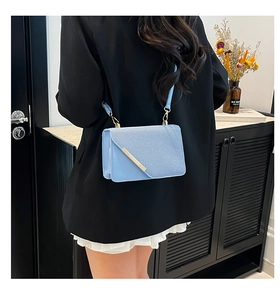 Détail du sac bandoulière bleu ciel avec bordure dorée porté par un mannequin en extérieur