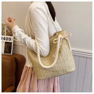 Close-up of woven straw shoulder bag featuring a lace bow and white thick rope handles
