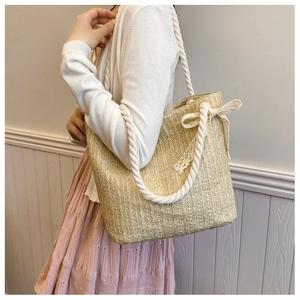 Detail of straw shoulder bag with thick rope handle and elegant lace bow decoration
