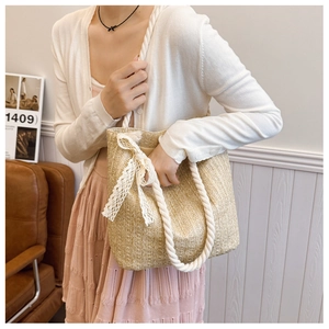 Close-up of straw tote bag with cotton rope handles and a white lace bow detail