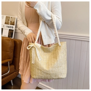 Detail of straw tote bag featuring thick cotton rope handles and delicate lace bow