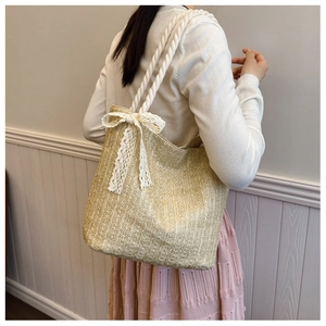 Detail of straw tote bag with lace bow decoration and rope straps shown on model
